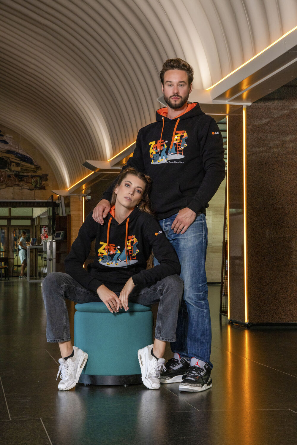 Two people wearing black custom hoodies with a colourful printed graphic, an example of branded merch that keeps being worn and seen long after a gift is delivered