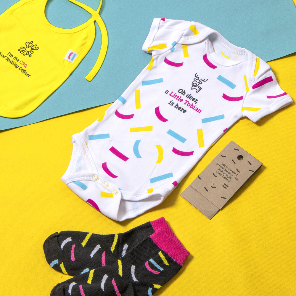 Ein individuelles Baby-Geschenkset mit einem Body, einem Lätzchen, Socken und einer Kraftpapier-Karte, ein Beispiel für ein momentbasiertes Geschenkprogramm, das ein Anbieter beherrschen sollte