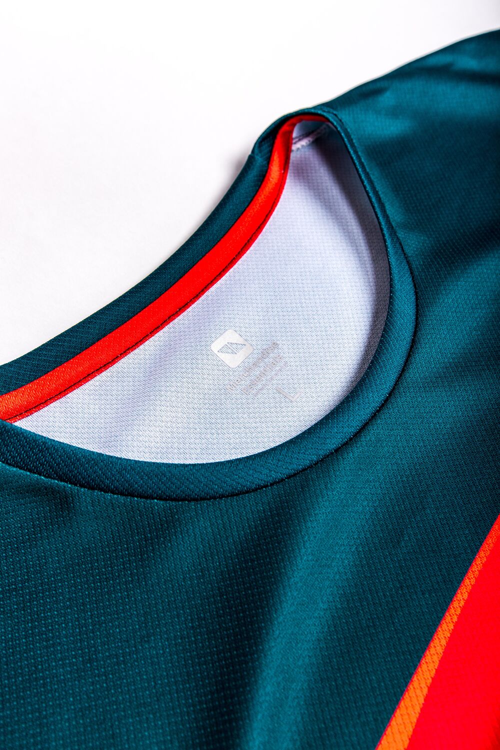 El cuello de un jersey deportivo azul verdoso y rojo mostrando la etiqueta de talla impresa por dentro, un recordatorio de que la curva de tallas pesa tanto como la elección de producto en las decisiones de stock