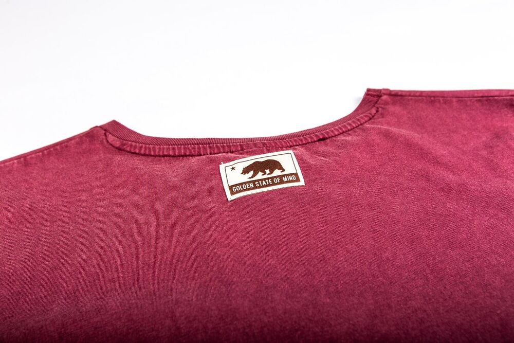 Back neck of a washed burgundy T-shirt with a printed 'Golden State of Mind' bear label below the collar