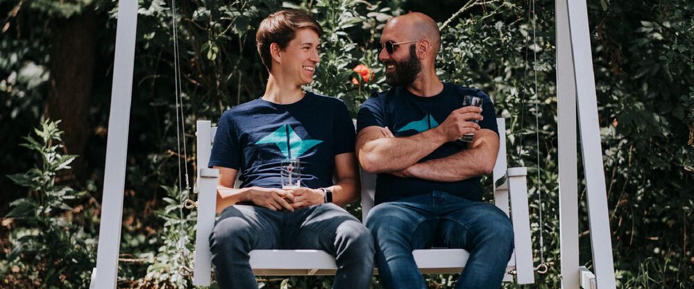 Dos compañeros sentados al aire libre en un banco de jardín con camisetas de la empresa