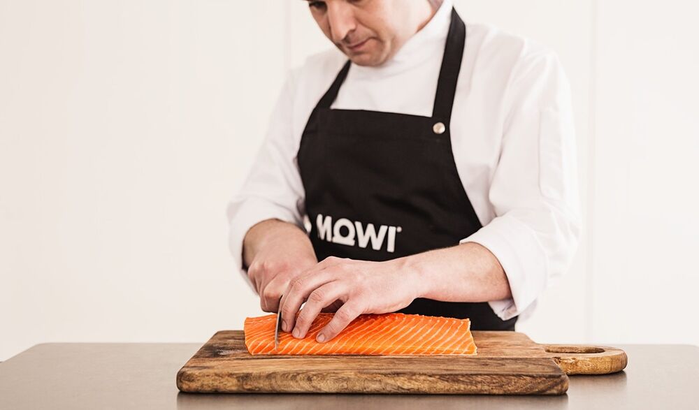 A chef working in a branded custom apron, an example of a centre-chest logo and a premium build worn in a real food environment