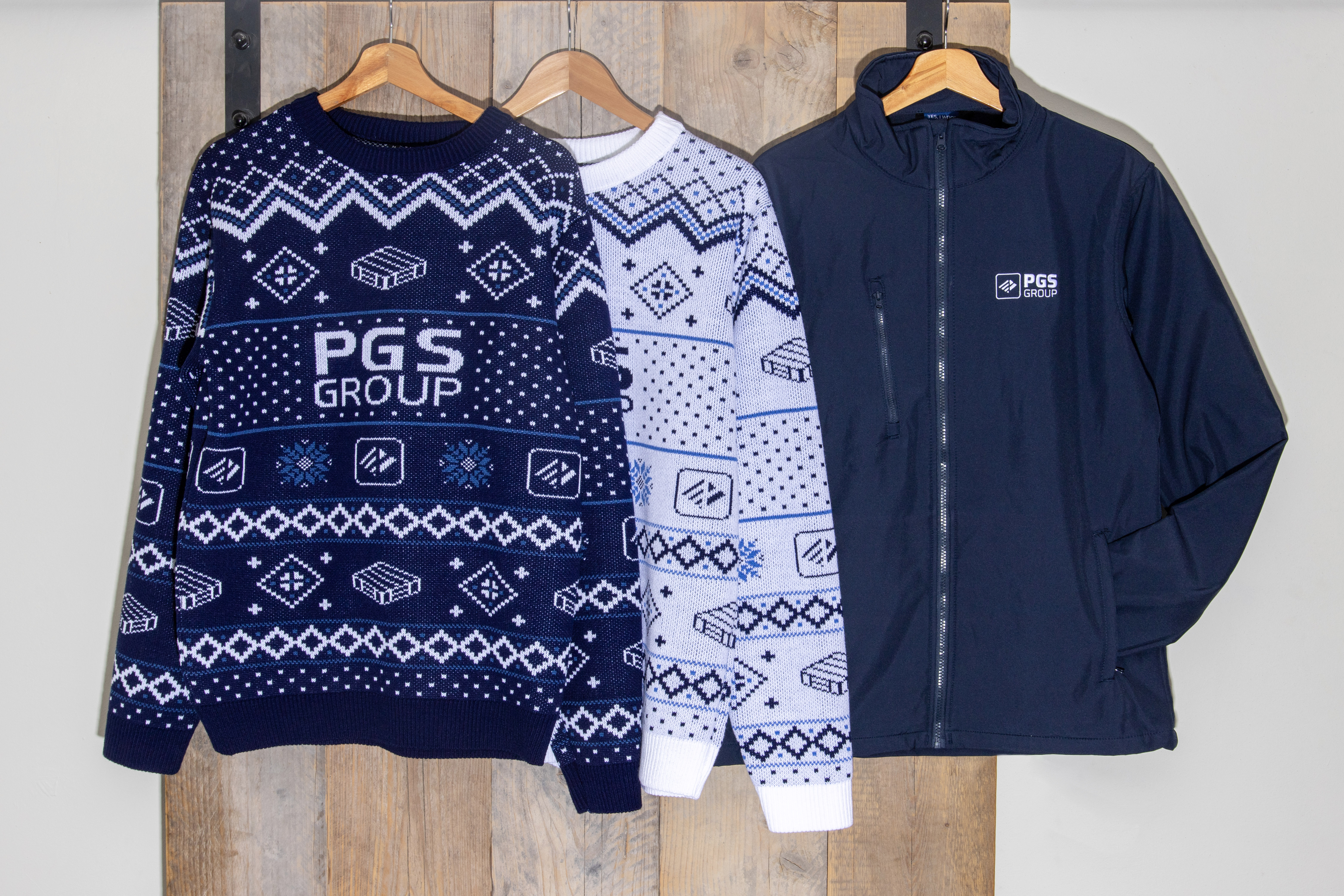 Drie gebrande kerstkleding-opties aan hangers: twee gepatroonde truien en een marineblauw ritsjack, voor PGS Group