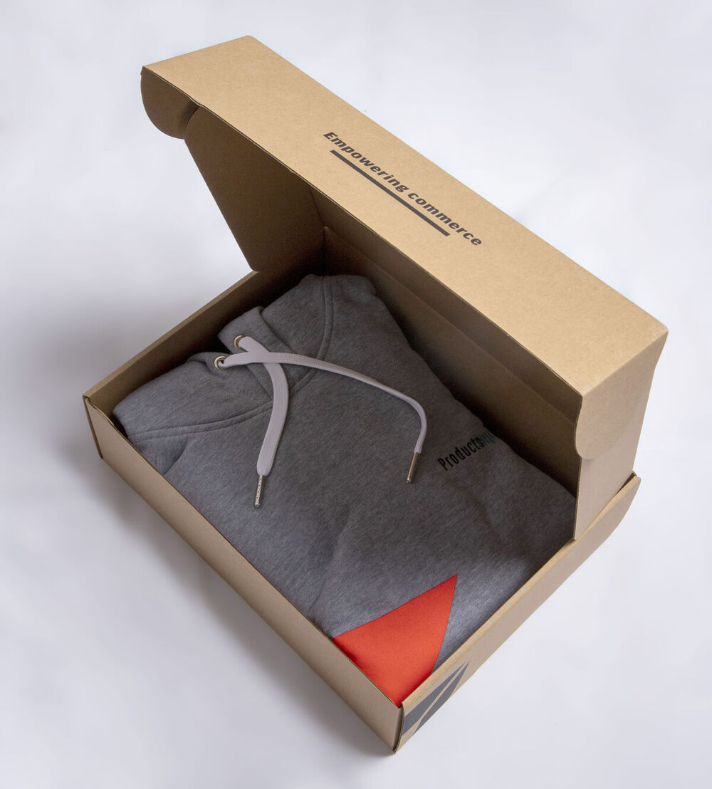 Open kraft box with 'Empowering commerce' printed inside the lid, holding a folded grey hoodie with an orange accent