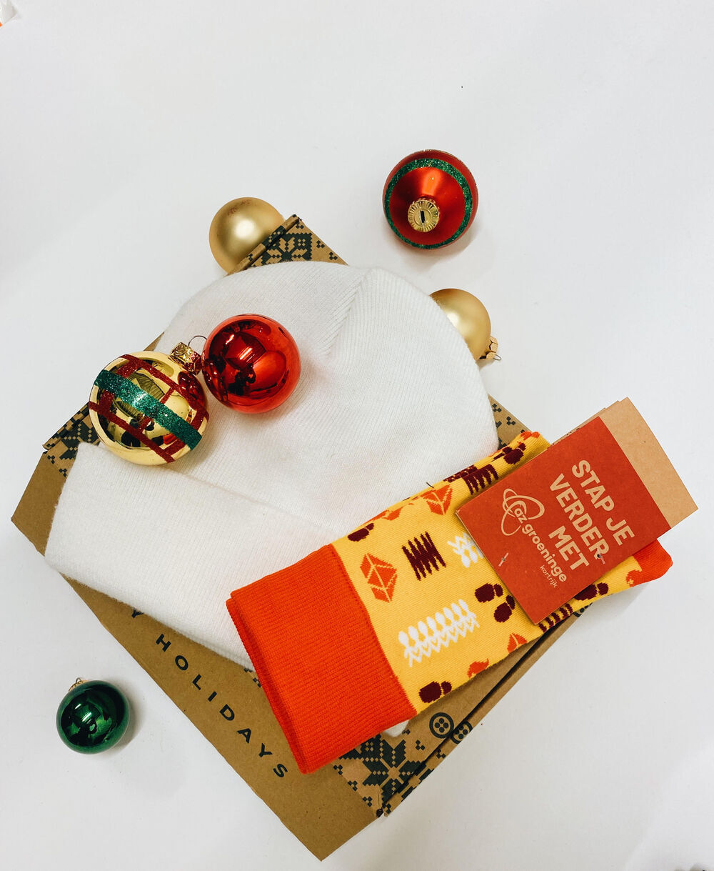 A kraft holiday gift box holding a white knitted beanie and a pair of patterned branded socks, the kind of seasonal kit that edible items can be added to
