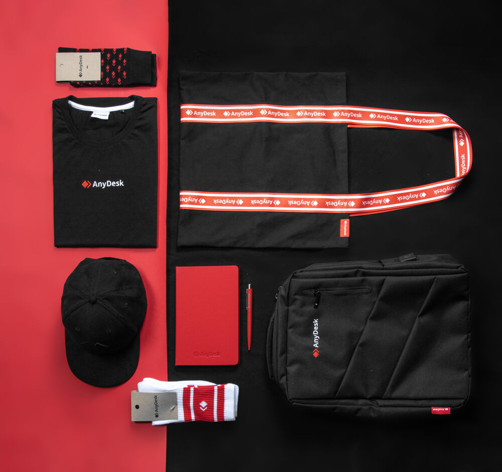 Una composición plana de un kit completo de bienvenida sobre fondo rojo y negro: calcetines, camiseta, gorra de marca, cuaderno y bolígrafo, mochila para portátil y lanyard