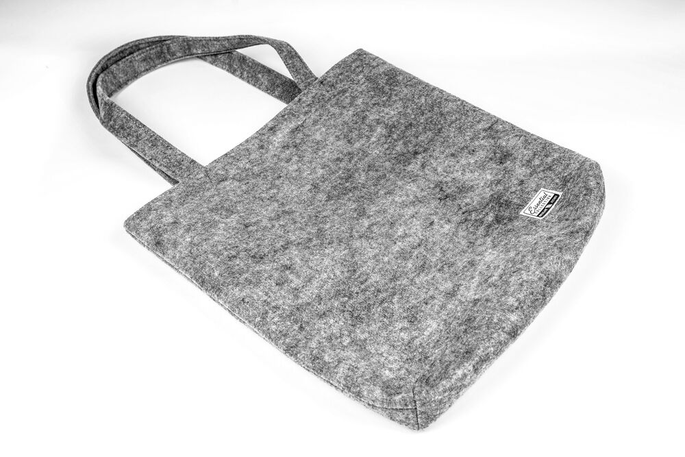 A grey felt tote bag with a small woven brand label, photographed on a plain white background
