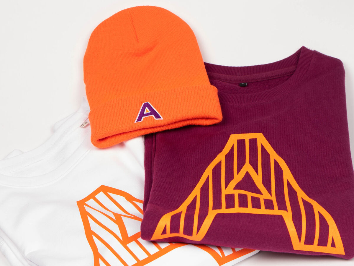 An expressive branded employee gift set laid out flat: a bright beanie and coordinated logo tees, the kind of internal collection employees are happy to wear
