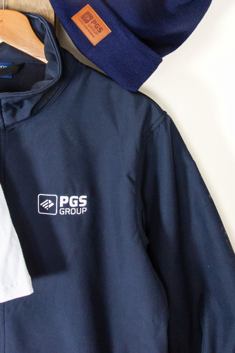 Una chaqueta softshell azul marino de marca con un logo bordado en el pecho, junto a un gorro azul marino a juego con un parche de cuero de marca