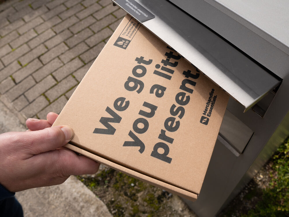 A kraft gift box printed with a short message being posted into a letterbox, showing a corporate gift addressed to a known recipient