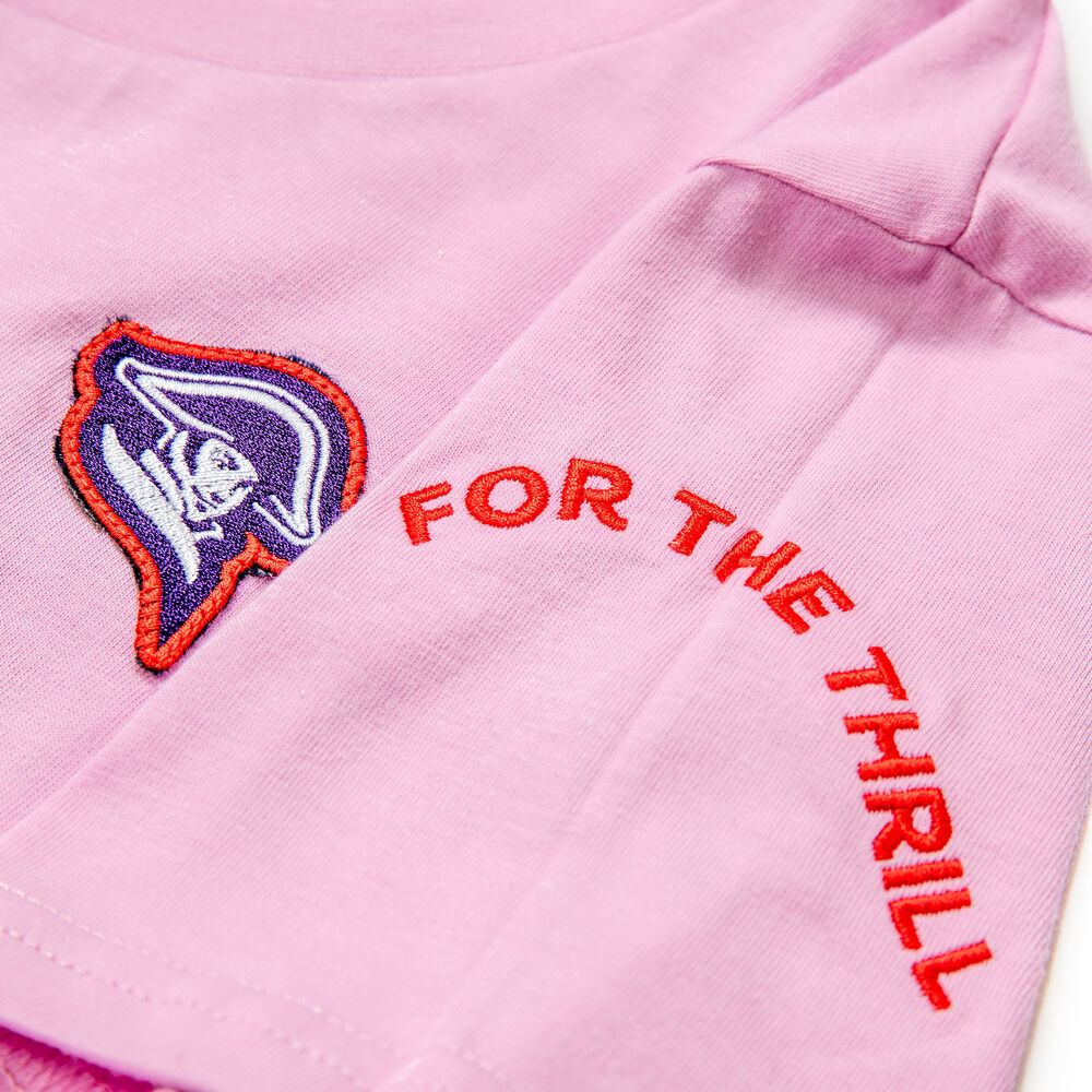 Close-up of a pink branded T-shirt showing an embroidered brand badge on the chest and an embroidered arc of text on the sleeve, two separate approved placements