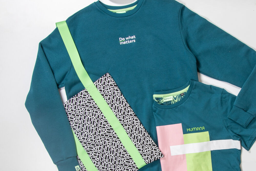 A teal branded sweatshirt with a patterned bag strap and a colour-blocked t-shirt laid flat, an example of a collection employees actually wear