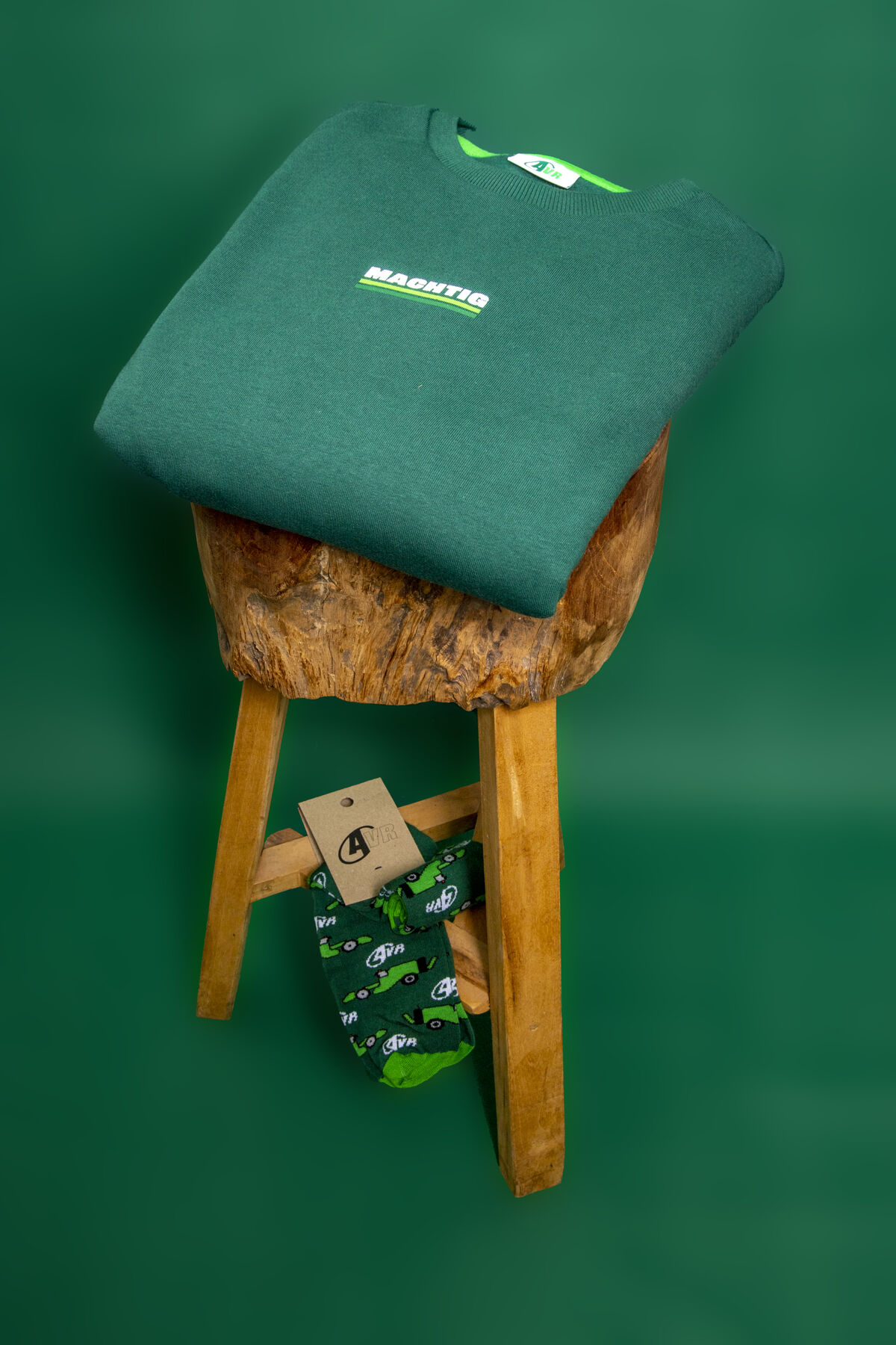 Una sudadera de marca verde oscuro doblada sobre un taburete de madera con calcetines a juego de marca con estampado de tractor, formando un set de activación listo para usar