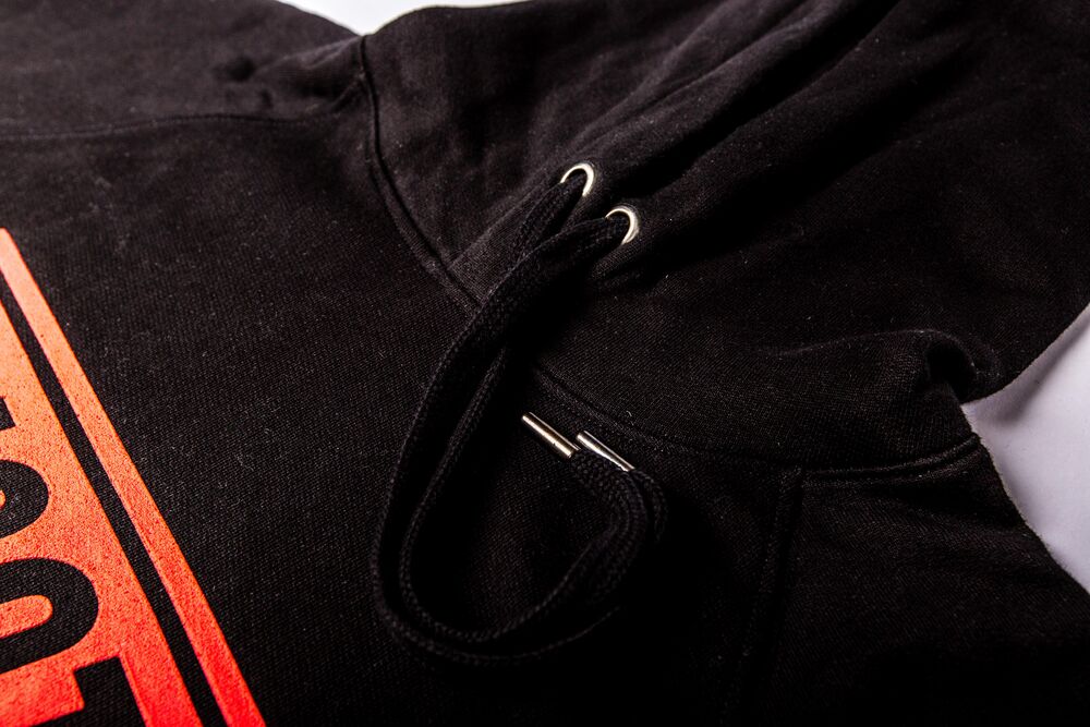 Detail of a black hoodie showing metal eyelets, a woven drawcord with metal tips and a clean pocket seam