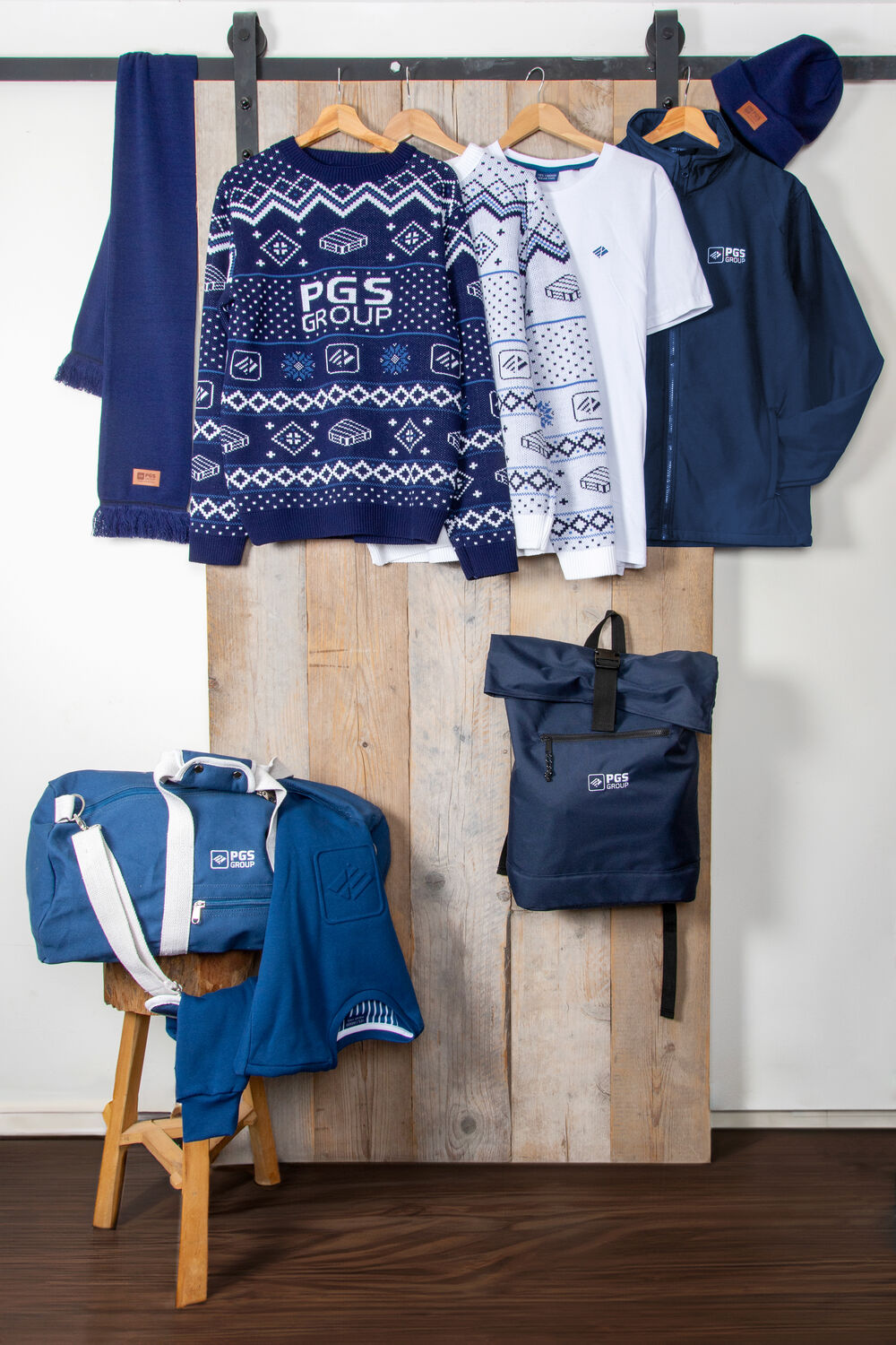 Eine vollständige Markenkollektion auf einer Kleiderstange: Schal, Strickpullover, Longsleeve, T-Shirt, Softshelljacke, Beanie, Sporttasche und Rucksack, alles in einer Markenidentität