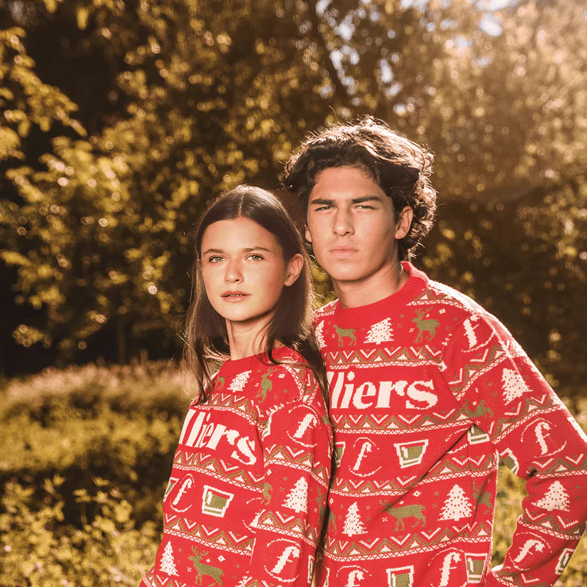 Twee werknemers dragen buiten bijpassende gebrande kersttruien, ontvangen als onderdeel van een cadeau-actie voor een verspreid team