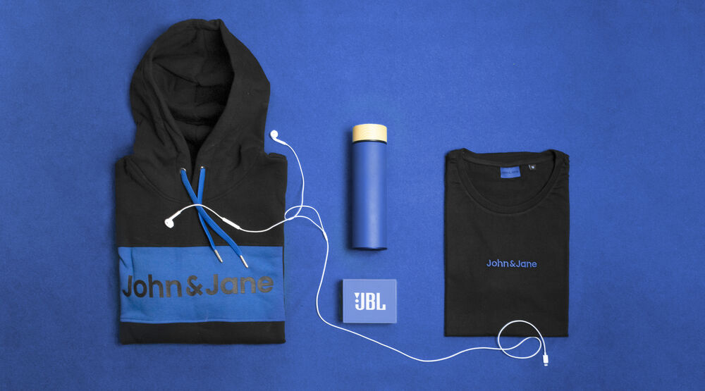 A branded hoodie, a bamboo-lidded bottle and a cotton t-shirt laid out on a blue backdrop, showing material choices in sustainable corporate gifts
