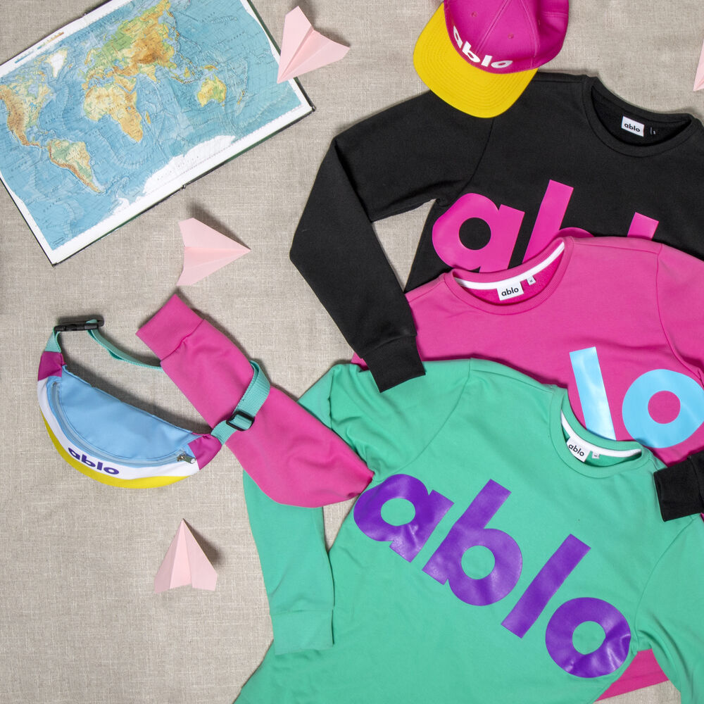 Eine Flat-Lay-Aufnahme einer vollständigen Markenkollektion mit Sweatshirts, einem T-Shirt, einer Cap und einer Gürteltasche in einer konsistenten Markenidentität